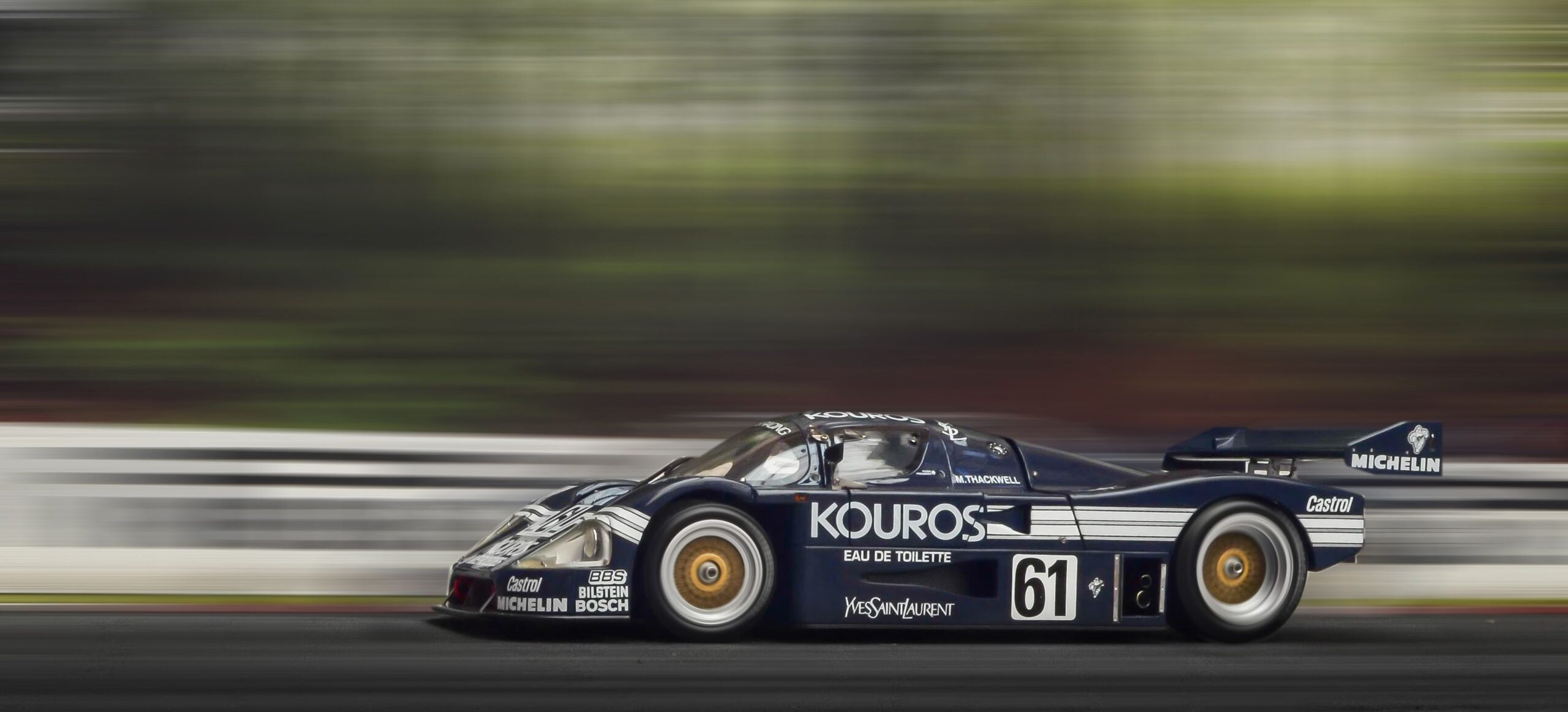 A race car at speed on a track, motion blurred, power committed to a line.