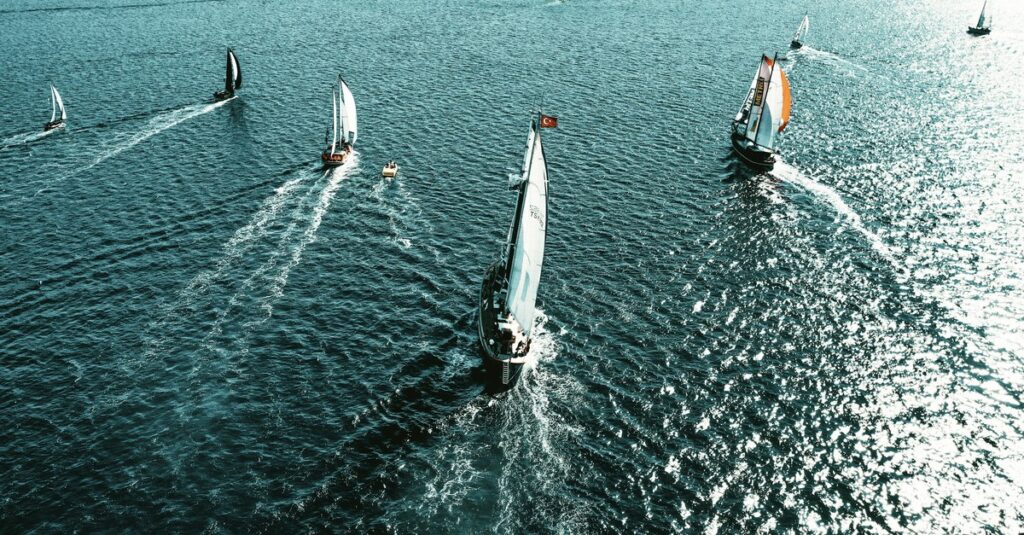 Aerial view of a sailboat fleet racing, each boat on its own heading across open water.