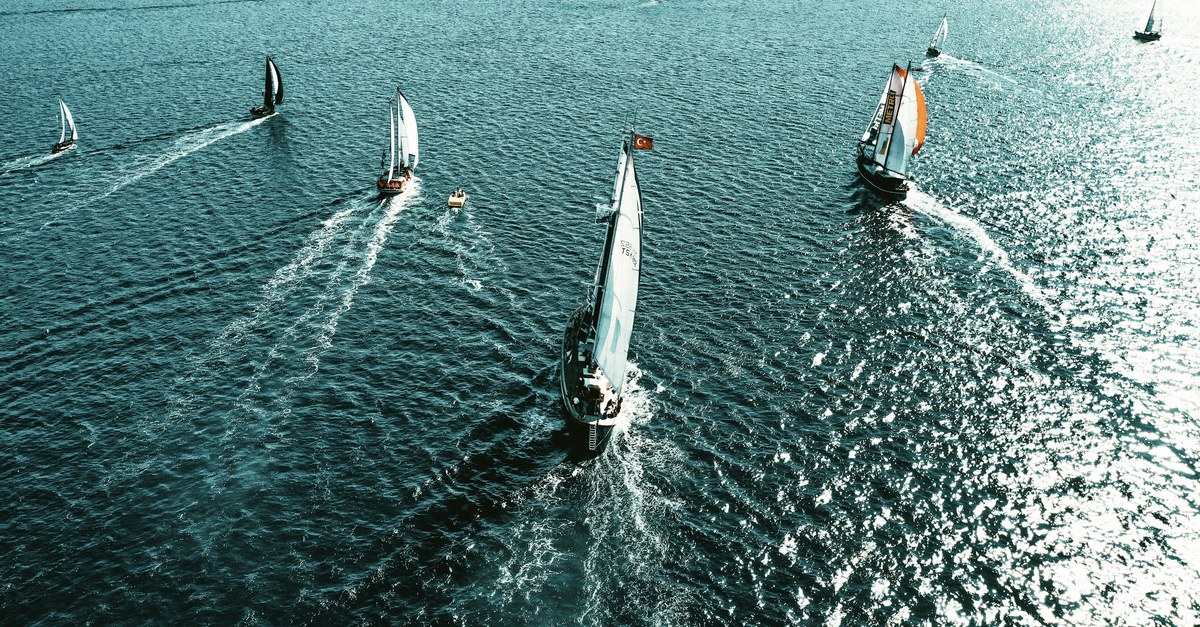 Aerial view of a sailboat fleet racing, each boat on its own heading across open water.