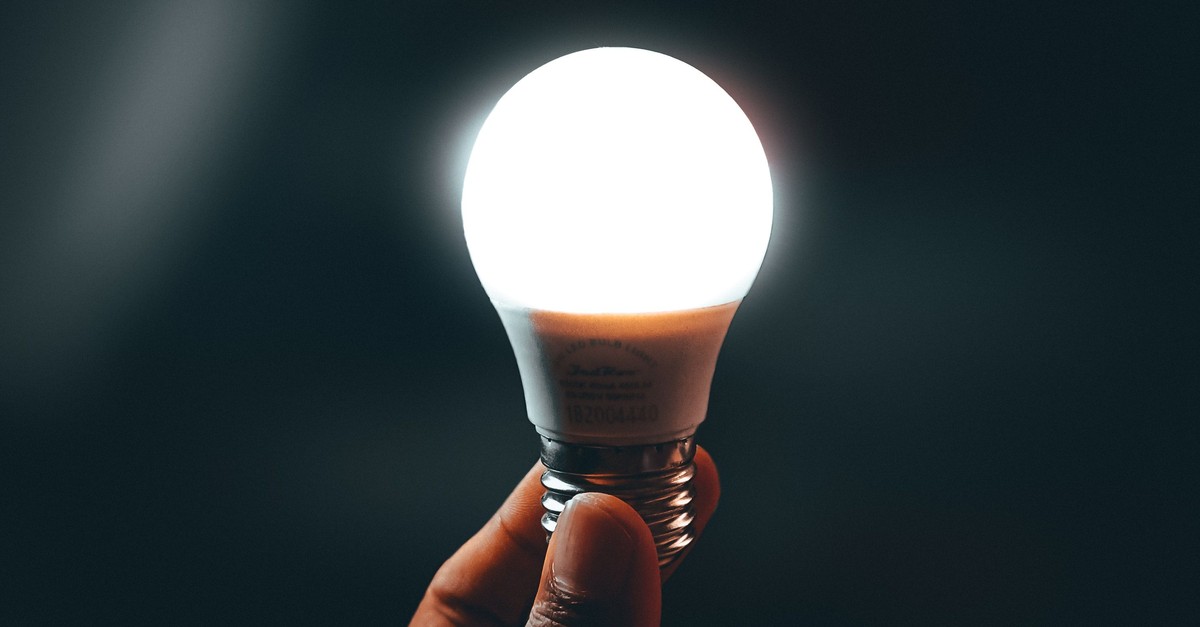 A single light bulb glowing bright white, held up by a hand against a dark background: a sudden burst of intelligence switched on.