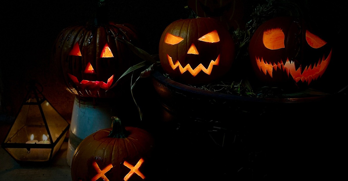 Carved jack-o'-lanterns glowing in the dark on a porch, each face cut a little differently.